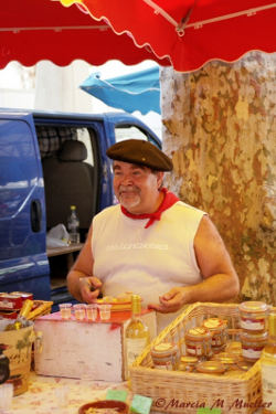 Plump honey vendor at St-Remy market, wearing black beret and red nickerchief, the inspiration for Maurice, photographed by Marcia M. Mueller.