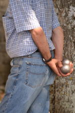  Man holding a pair of boules, steel balls about the size of tennis balls, behind his back.